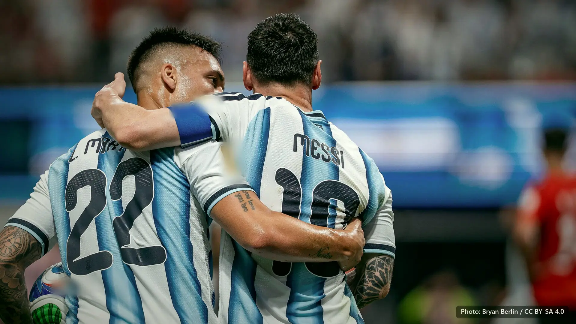 Lautaro Martinez with his arm around Messi, both seen from behind in Argentina stripes.