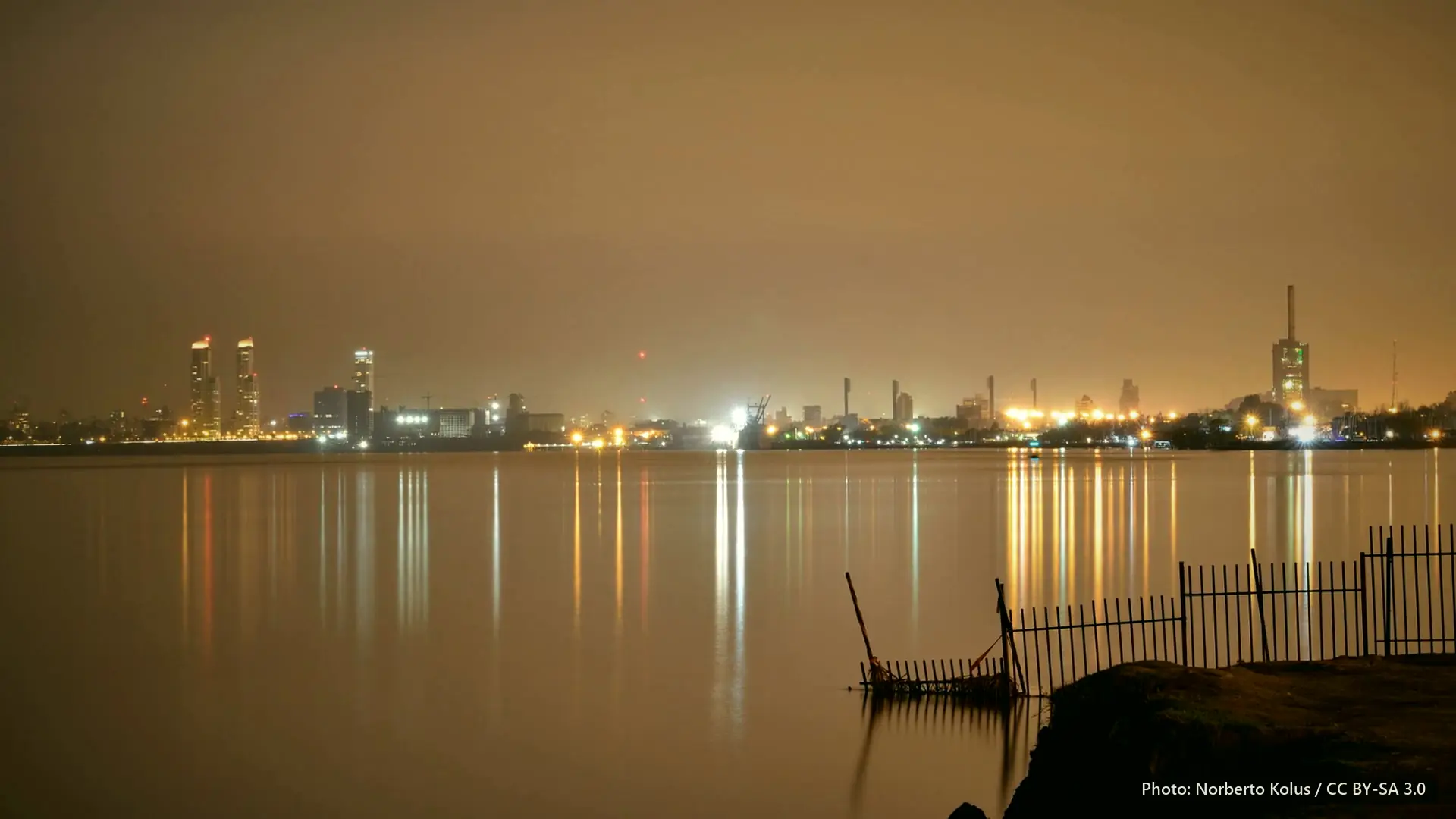 The Rosario riverfront at night, with lights across the water under an orange sky.